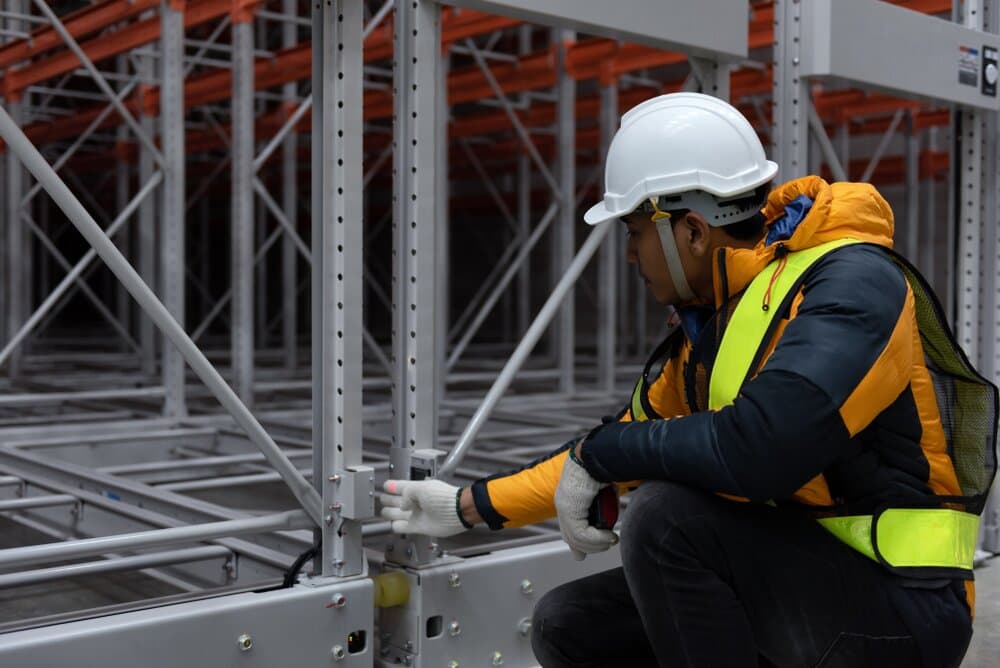 Worker in a hard hat and safety vest inspecting a storage rack