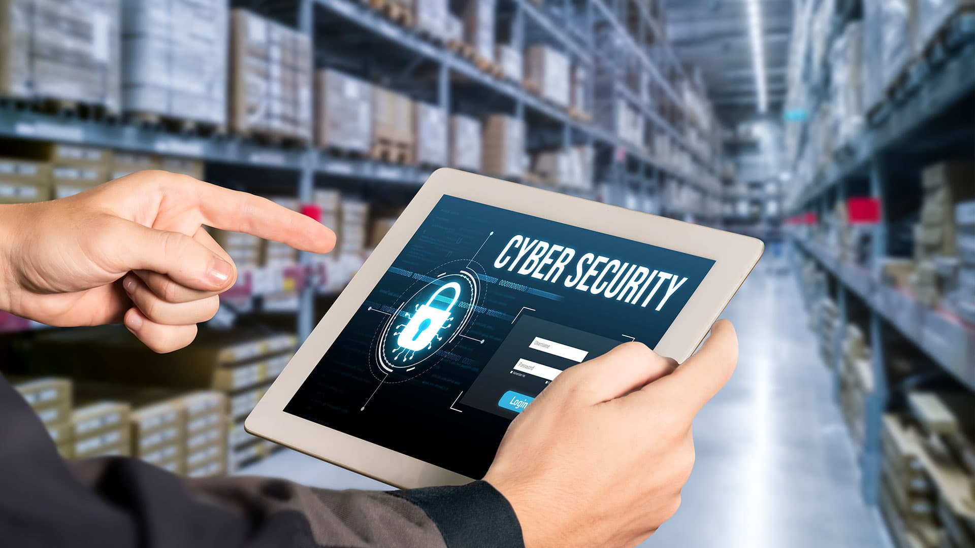 Hand pointing at a tablet displaying a cyber security login screen with a padlock icon, warehouse racking blurred in background.